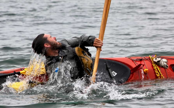A person practices a wet exit in a kayak on a body of water. 